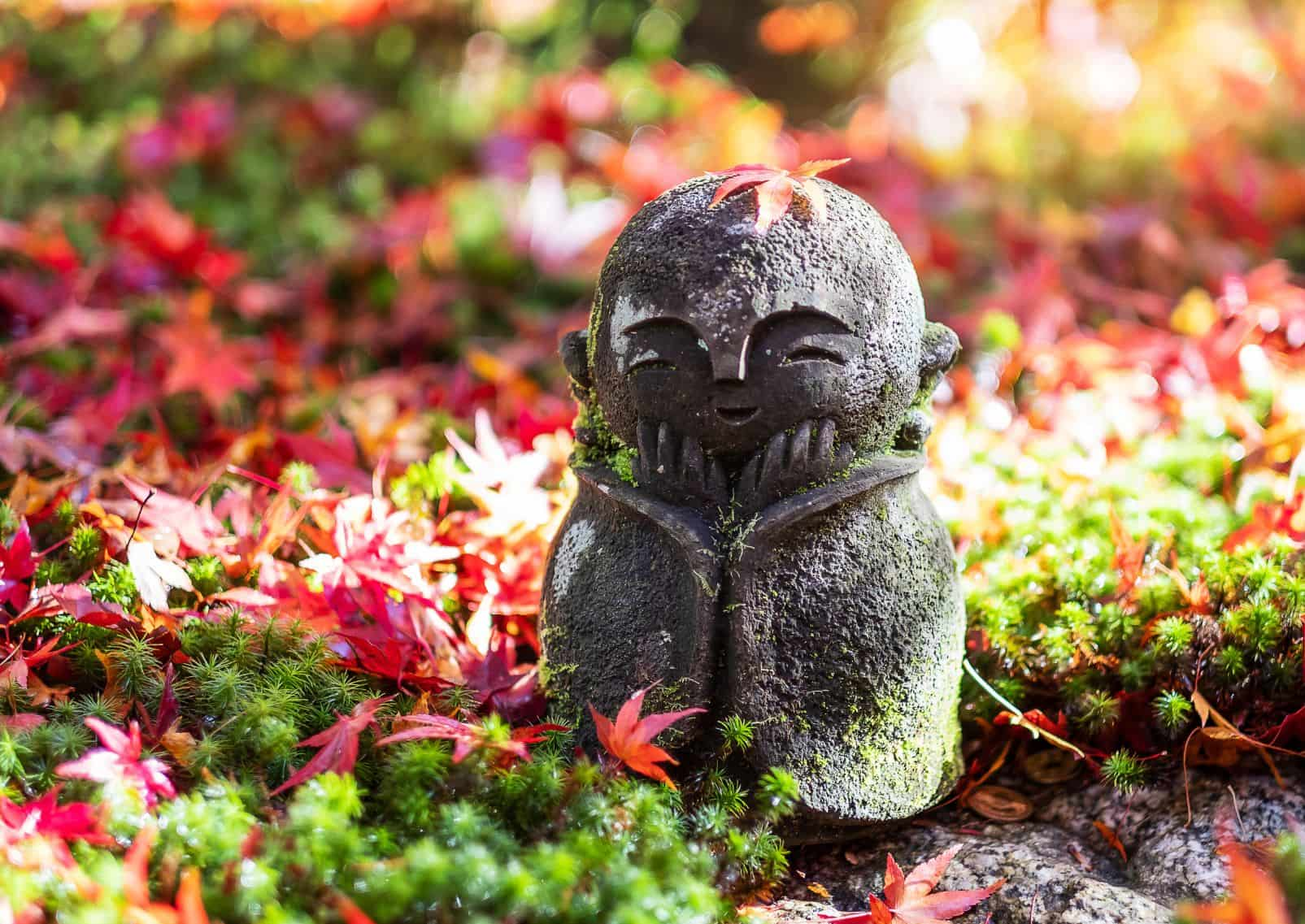 Japán jizo-szobor vörös juharlevelek között az Enkoji templom japánkertjében, Kiotó, Japán