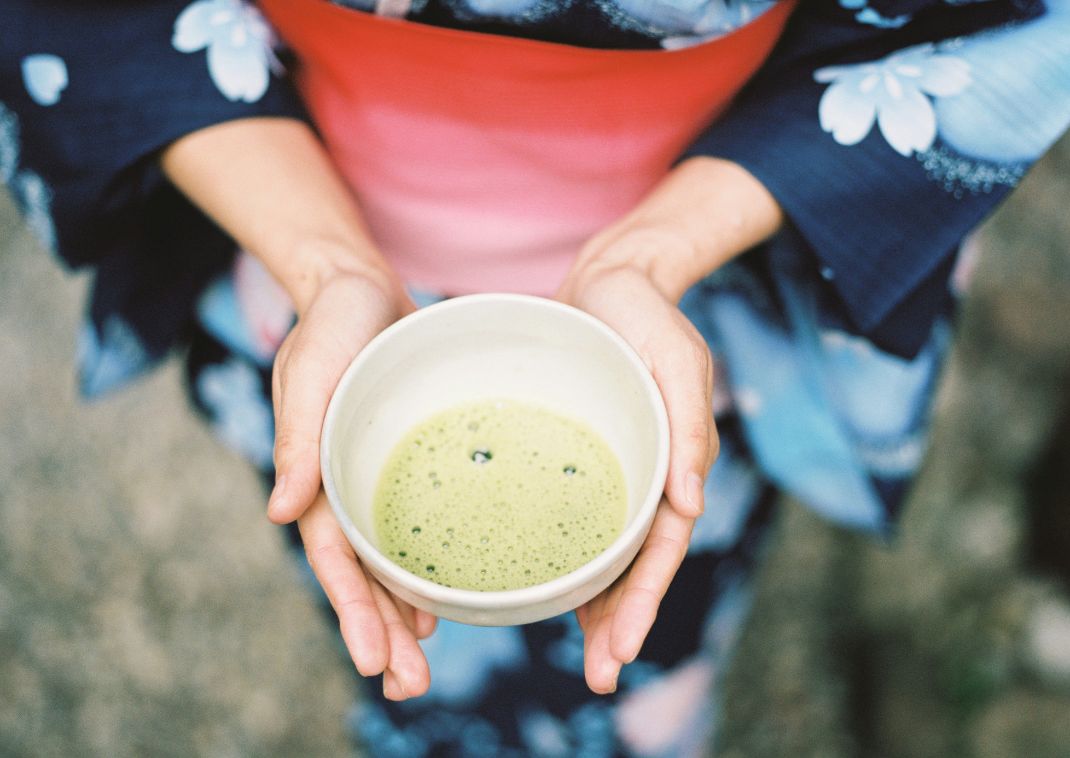 Egy yukatát viselő nő egy csésze matcha teát tartva