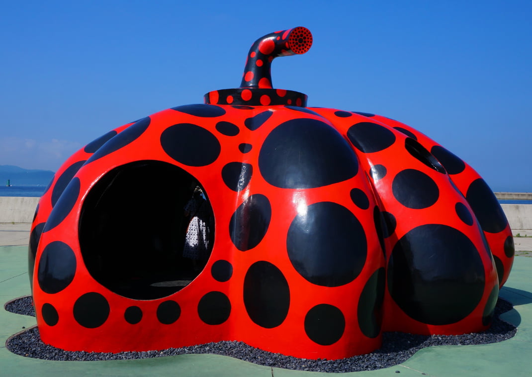 Yayoi Kusama világhírű piros tök szobra fekete pöttyökkel, Naoshima szigetén, tiszta kék ég alatt, a tengerpart közelében.