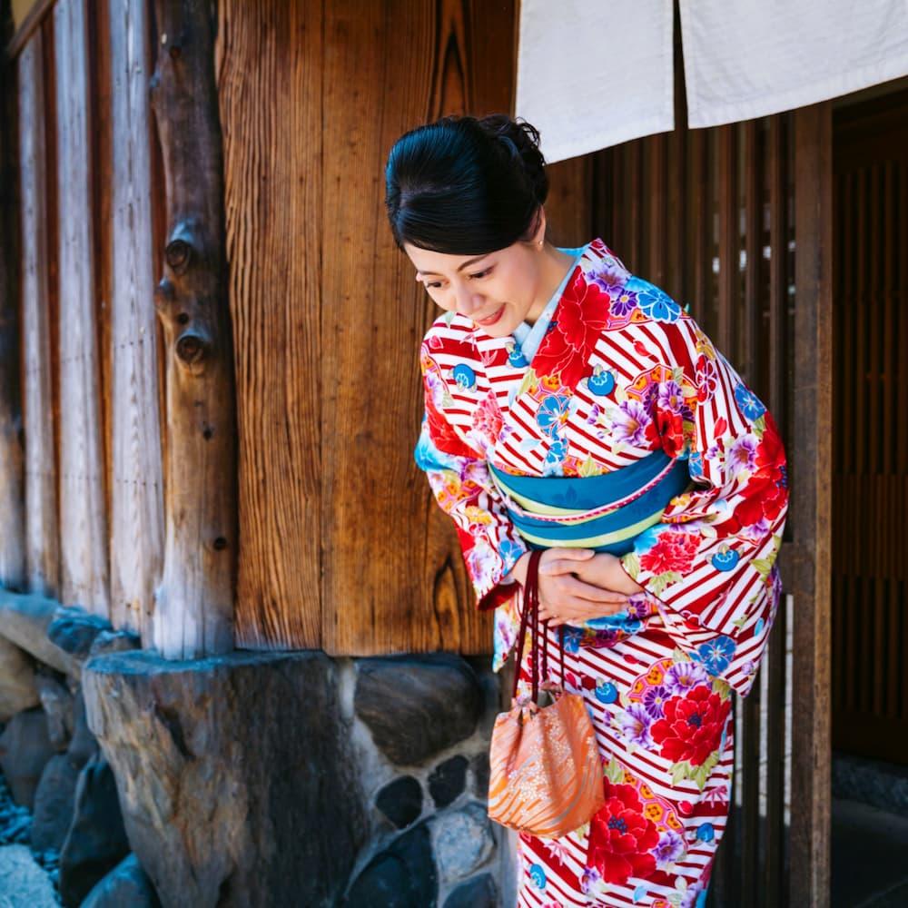 Japán nő színes kimonóban meghajol egy hagyományos faépület előtt Kiotóban