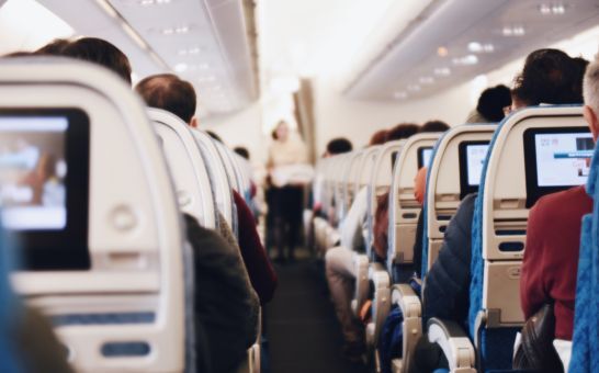 Egy nagy utasszállító repülőgép belseje, az emberek ülnek, és egy egyenruhás stewardess sétál a folyosón