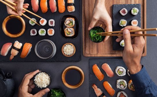Válogatott sushi, beleértve a nigirit, sashimit és tekercseket, amelyeket pálcikákkal osztanak meg és esznek.