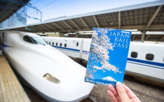 Egy Japán vasúti bérletet tartó kéz egy Shinkansen előtt a tokiói pályaudvaron