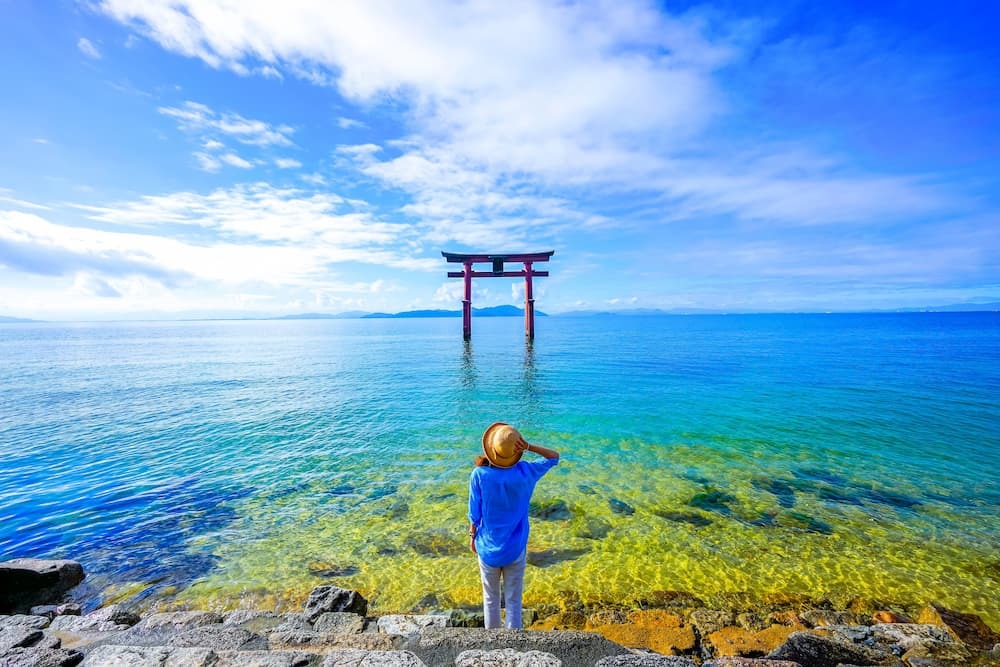Utazó áll egy torii kapu mellett a Biwa-tónál, Shiga prefektúra, Japán