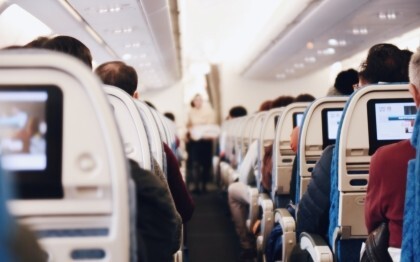 Egy nagy utasszállító repülőgép belseje, az emberek ülnek, és egy egyenruhás stewardess sétál a folyosón
