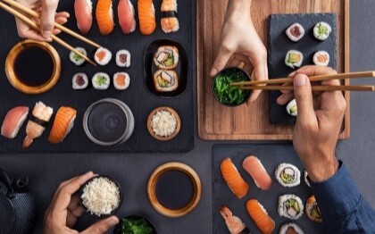 Válogatott sushi, beleértve a nigirit, sashimit és tekercseket, amelyeket pálcikákkal osztanak meg és esznek.