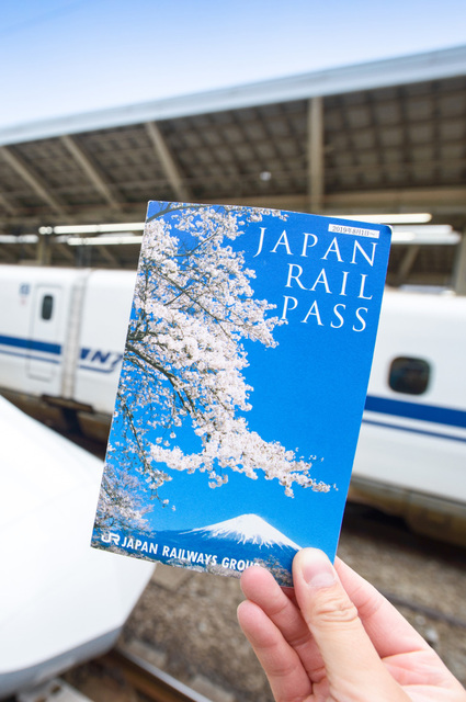 Egy Japán vasúti bérletet tartó kéz egy Shinkansen előtt a tokiói pályaudvaron