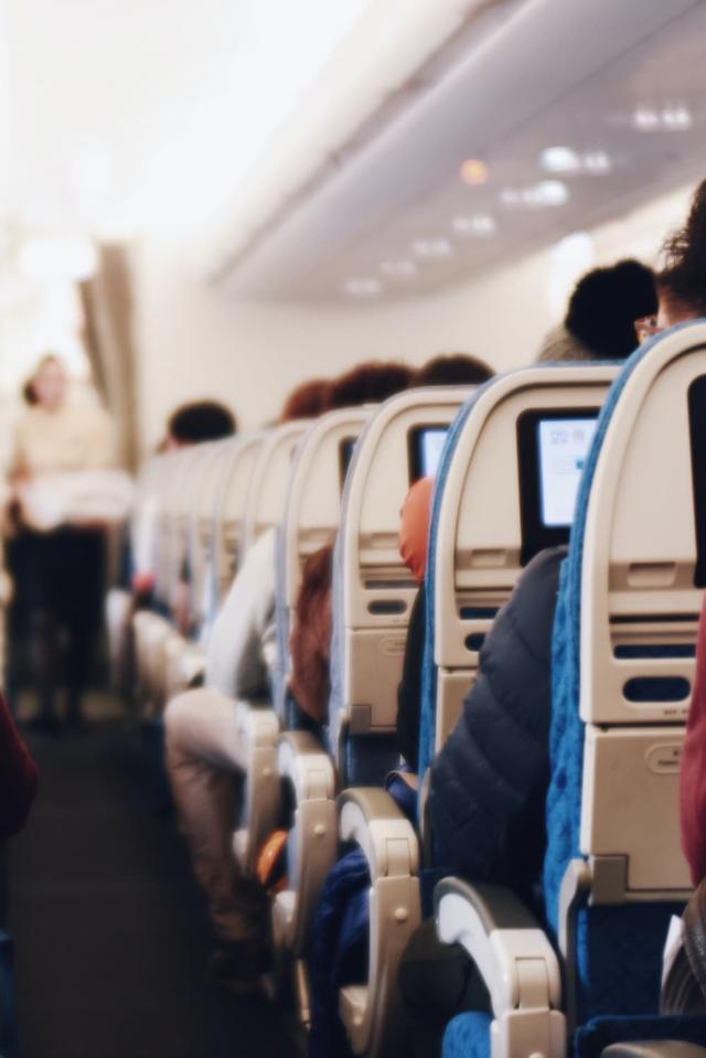 Egy nagy utasszállító repülőgép belseje, az emberek ülnek, és egy egyenruhás stewardess sétál a folyosón