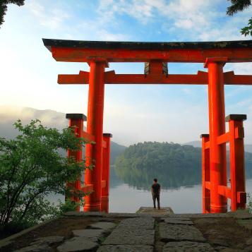 Turista az Ashi-tónál található Hakone szentély vörös torii kapujánál, Japánban